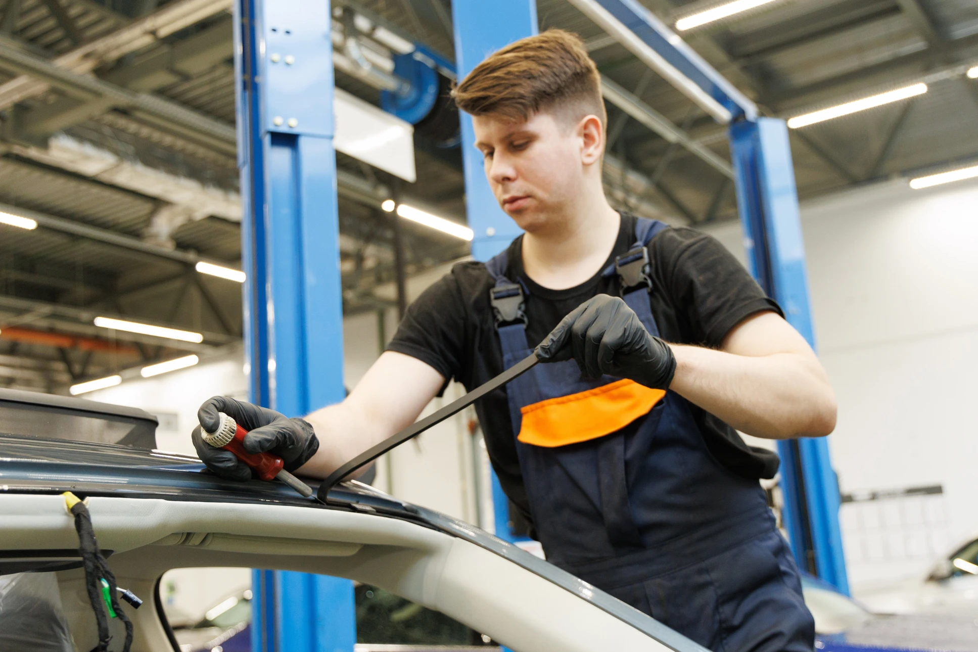 Jeune technicien automobile travaillant dans un garage moderne équipé de ponts élévateurs bleus