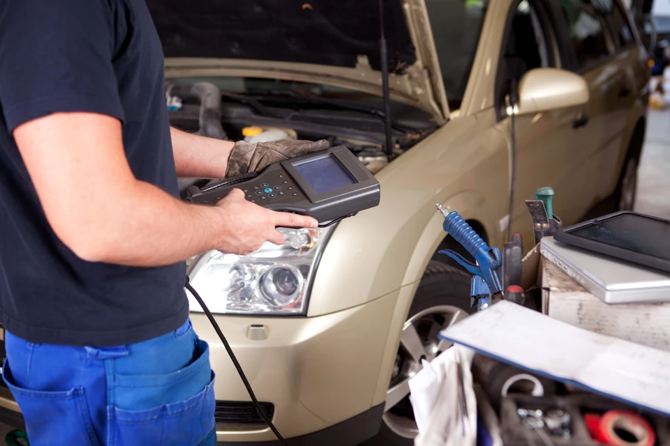 Technicien automobile en combinaison de travail et casquette effectuant un diagnostic sur véhicule blanc dans un garage moderne